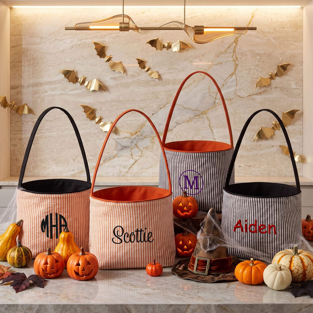 Four personalized Halloween bucket bags arranged on a marble surface with Halloween decorations.