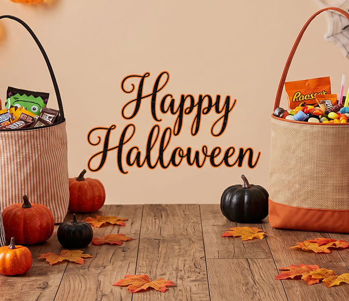 Five Halloween candy baskets arranged on a wooden table with pumpkins, autumn leaves