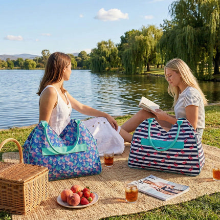 Two women sitting by a lake with picnic bags and food.