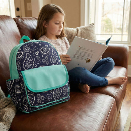 Girl reading a book on a couch next to a navy-white paisley print backpack